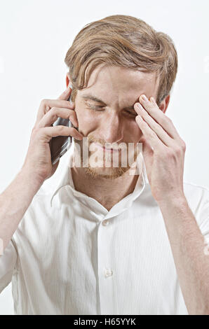 Jeune adulte Homme en chemise blanche à l'écoute de son téléphone, de toucher sa tête avec une main, la réception de mauvaises nouvelles Banque D'Images