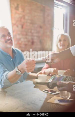 Serveur avec lecteur de carte de crédit donnant à l'homme tout à la réception au restaurant table Banque D'Images