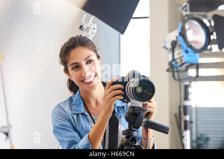 Femme photographe souriant derrière appareil photo en studio Banque D'Images