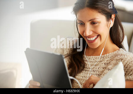 Smiling woman using digital tablet with headphones on sofa Banque D'Images