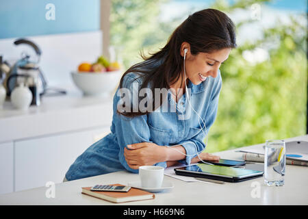 Smiling woman écoutez de la musique avec des écouteurs et un lecteur mp3 dans la cuisine Banque D'Images