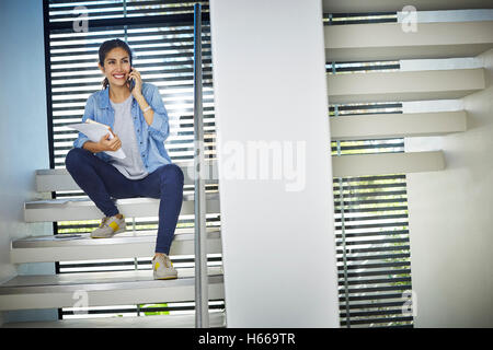 Smiling businesswoman with paperwork in escalier moderne Banque D'Images