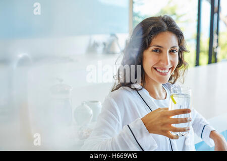 Portrait of smiling woman in bathrobe drinking water in kitchen Banque D'Images