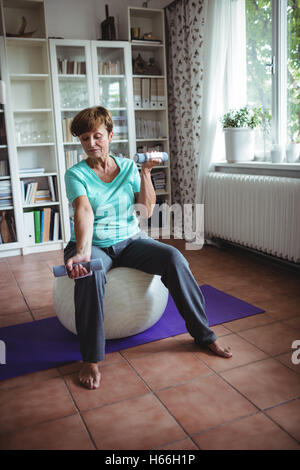 Senior woman exercising with dumbbells sur boule d'exercice Banque D'Images