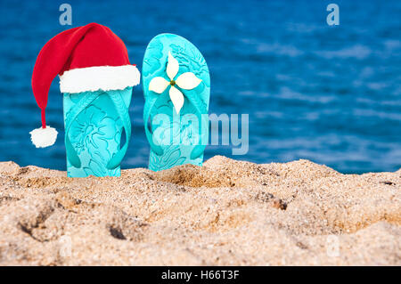 Chapeau de Noël sur tongs dans le sable d'une plage Banque D'Images