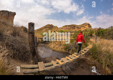 Femme hiker crossing pendaison, passerelle suspendue le ruisseau, dans le majestueux Golden Gate Highlands National Park, Afrique du Sud. Banque D'Images