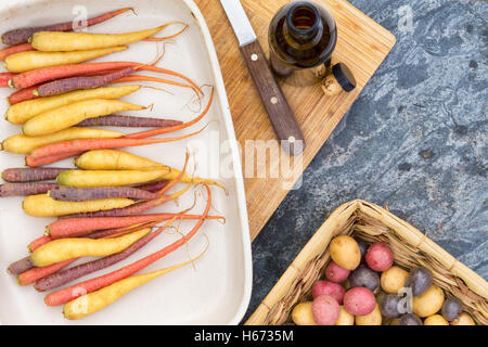 Rouge, orange, jaune et violet les carottes et les pommes de terre avec la planche à découper et couteau de haut en bas première personne Banque D'Images