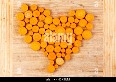 Produits frais en fines rondelles les carottes orange disposés en forme du cœur formé des valeurs d'obus sur une planche à découper en bambou, con Banque D'Images