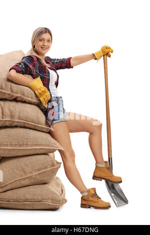 Portrait d'une productrice appuyée sur une pile de sacs de toile et tenant une pelle isolé sur fond blanc Banque D'Images