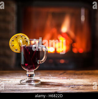 Vin chaud avec tranche d'orange, clous de girofle et le bâton de cannelle. Cheminée avec feu chaud sur l'arrière-plan. Banque D'Images