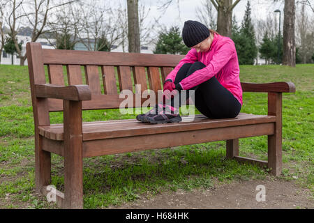 Jeune femme athlète fatigué ou déprimé se reposant sur un banc sur une froide journée d'hiver de la piste d'un parc urbain. Banque D'Images