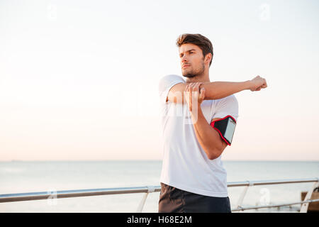 Jeune homme musclé s'étendant ses bras en position debout au bord de la mer Banque D'Images