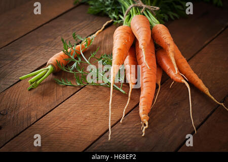 Botte de carottes fraîches avec des feuilles vertes sur fond de bois. Banque D'Images