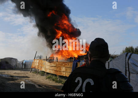 Calais, France. 25 octobre, 2016. Un agent de police watches la cabane brûler. Le deuxième jour de l'expulsion de la Jungle à Calais a vu le démarrage de la démolition de la jungle. Certains refuges ont été démolis par des ouvriers, tandis que d'autres refuges ont été délibérément brûlés. Crédit : Michael Debets/Pacific Press/Alamy Live News Banque D'Images