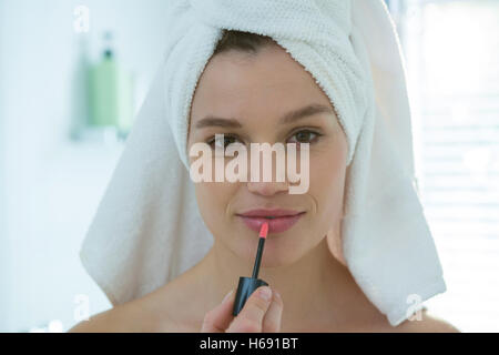 Woman applying lip gloss sur ses lèvres dans la salle de bains Banque D'Images