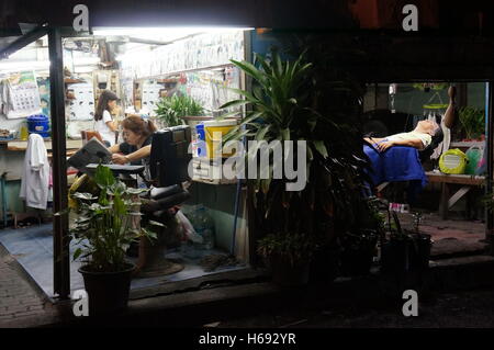 Une famille de coiffeurs travaillant de nuit, une scène de la vie de rue à Bangkok dans les jours qui suivent la mort du roi Rama IX. Banque D'Images