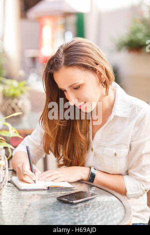 Jeune femme écrivant dans son portable assis à la table in restaurant Banque D'Images