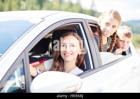 Jeune femme et ses enfants assis dans une voiture et regarder dehors à partir de windows. Voyages en famille image en arrière-plan Banque D'Images