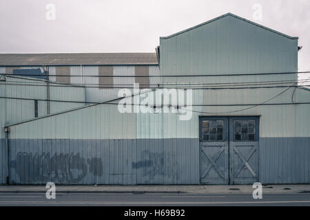 Ancien entrepôt peint en bleu et gris avec des graffitis nettoyage et de belles portes et fenêtres couvertes sur une journée nuageuse Banque D'Images