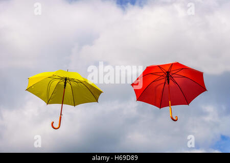 Parapluie rouge et jaune ou des parasols en suspension dans l'air flottant sous ciel nuageux Banque D'Images