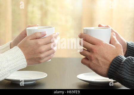 Profil des mains d'un couple holding les tasses de café sur une table en hiver dans un appartement avec une fenêtre à l'arrière-plan Banque D'Images