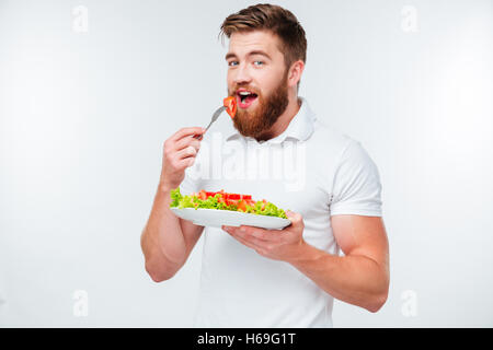 Jeune homme barbu eating salad isolé sur fond blanc Banque D'Images