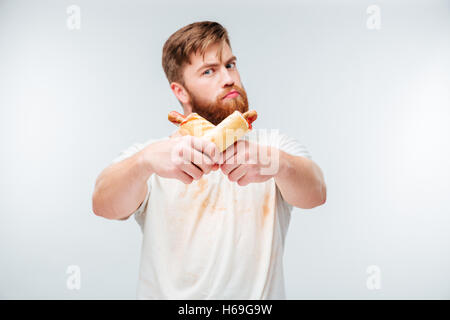 Jeune homme barbu en chemise sale tenant deux hot-dogs isolé sur fond blanc Banque D'Images