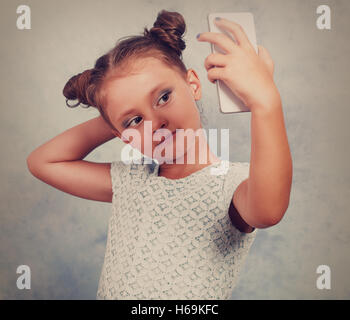 Fun kid girl posing et prendre une photo selfies sur téléphone mobile. Vintage portrait tonique Banque D'Images