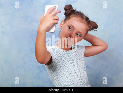 Fun kid girl posing et faire une photo sur téléphone mobile selfies sur fond bleu Banque D'Images