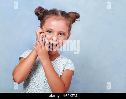 Heureux kid girl talking on mobile phone avec bouche ouverte sur fond bleu avec copie espace vide. closeup portrait Banque D'Images