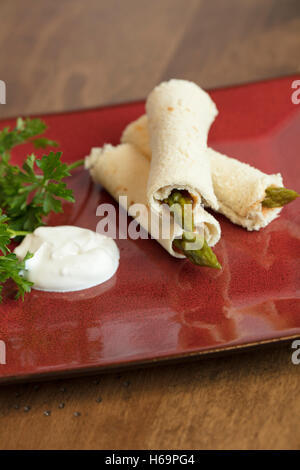 Les asperges roulées dans du pain aplati avec une vinaigrette russe et la crème sure garni de persil Banque D'Images