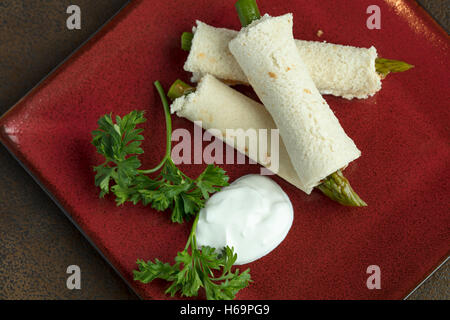 Les asperges roulées dans du pain aplati avec une vinaigrette russe et la crème sure garni de persil Banque D'Images