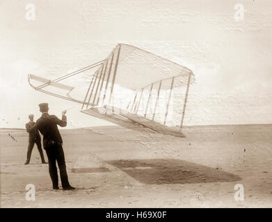 Vue latérale du planeur voler comme un cerf-volant près du sol, Wilbur et Orville à gauche à droite, vers l'avant du planeur à droite et incliné vers le bas. Banque D'Images