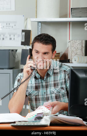 Homme assis au bureau, au téléphone, holding graphiques en couleurs Banque D'Images