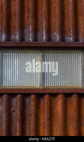 Close Up de métal ondulé rouillé mur avec deux briques de verre texturé dans le centre Banque D'Images