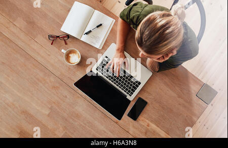 Vue de dessus de woman using laptop while sitting at cafe table avec ordinateur portable, téléphone mobile, journal, tasse à café et verres. Surf féminin Banque D'Images