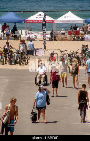 Un vétéran handicapé en fauteuil roulant d'une compétition de surf visites à Huntington Beach, CA. Remarque les auvents et signes en arrière-plan. Banque D'Images