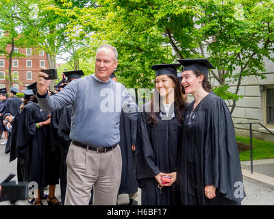 À l'aide d'un téléphone cellulaire, un fier père prend une photo de selfies avec sa fille et son meilleur ami de l'Asie dans l'obtention du diplôme de capuchons et de robes le jour de la remise des diplômes à l'Université de Harvard à Cambridge, MA. Banque D'Images