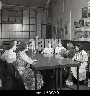 Années 1950, historiques, réunion du personnel. Jeune femme office personnel de l'usine s'asseoir autour d'une table d'avoir une discussion informelle avec un directeur d'entreprise, England, UK. Affiche sur un mur dit que nous vivons par les exportations". Banque D'Images