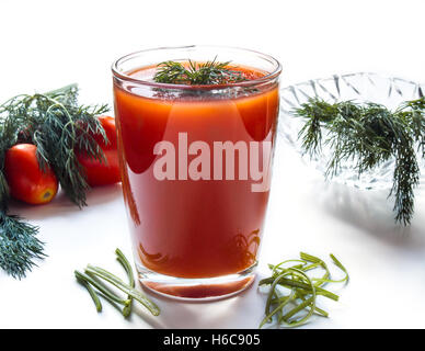 Du jus de tomates dans un grand verre sur un fond blanc avec des herbes et des tomates Banque D'Images