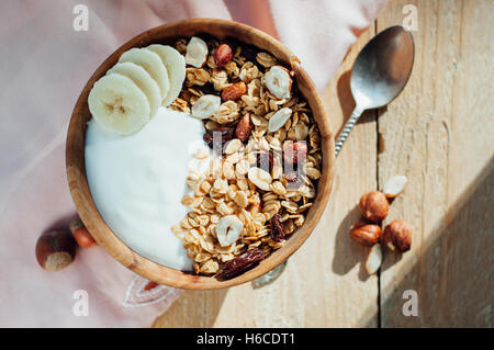 L'avoine avec granola maison les noix, les raisins et les bananes dans un bol en bois, matin ensoleillé Banque D'Images