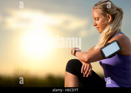 Portrait de jeune athlète contrôle d'entraînement sur smart watch au coucher du soleil.Femme portant brassard avec smart watch. Banque D'Images