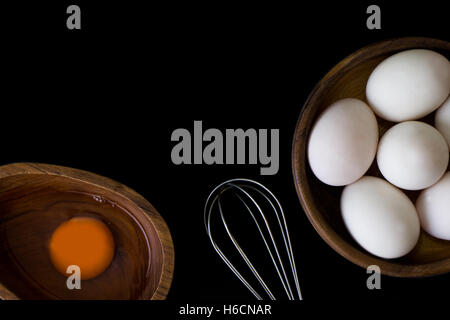 En bois blanc d'oeuf dans un bol et fouetter en teck sur fond noir Banque D'Images
