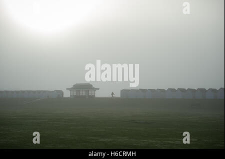 Une personne marche entre les cabines de plage et un abri sur la promenade en front de mer à Goring par mer dans le West Sussex, Angleterre. Banque D'Images