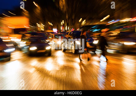 Photo avec l'appareil photo fait effet de zoom de personnes traversant une rue la nuit Banque D'Images