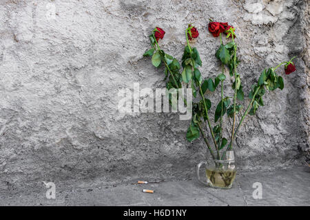 Roses de mourir abandonnés sur le sol dans une tasse avec de l'eau sale Banque D'Images