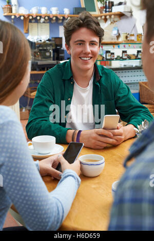 Groupe d'amis adolescents réunion dans un café et l'utilisation de téléphones mobiles Banque D'Images