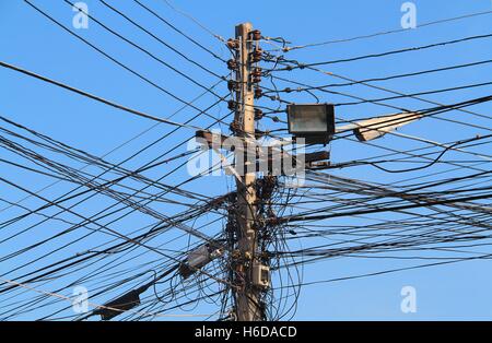 Un lampadaire de rue avec de nombreux câbles électriques qui fonctionnent dans des directions différentes sur fond de ciel bleu Banque D'Images