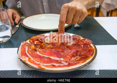 La main de l'homme ayant une assiette de chorizo ibérique de variétés de produits. L'Espagne. Banque D'Images