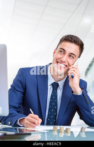 Close up portrait of handsome young businessman talking on smart phone in office. Jeune homme au bureau devant l'ordinateur. Banque D'Images